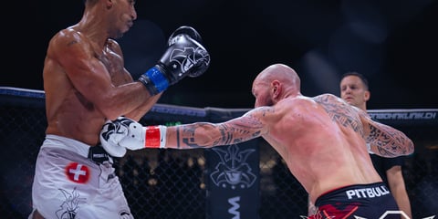 Two shirtless male boxers fighting in a ring during a professional boxing match, one wearing blue gloves and the other in red.