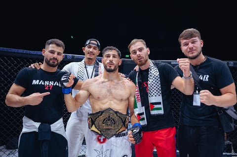 MMA fighter in victory pose with championship belt surrounded by team members in octagon ring