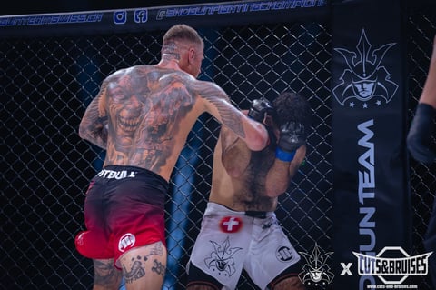 Two shirtless MMA fighters in an octagon cage during a professional fight, one throwing a punch at the other.