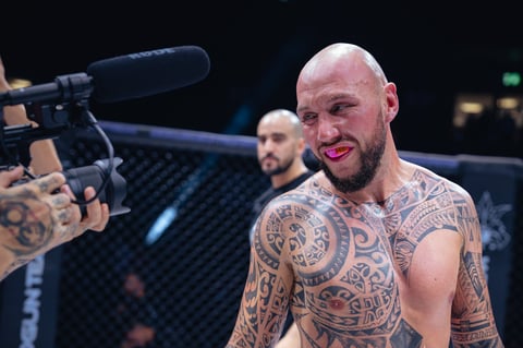 Bald tattooed man being interviewed with microphone in MMA octagon cage