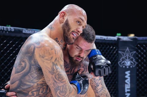 Two tattooed male fighters grappling inside an octagon cage during a mixed martial arts competition