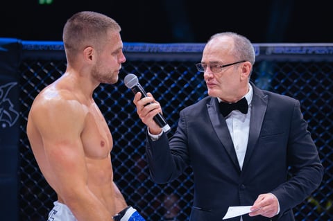 MMA fighter shirtless in octagon speaking with suited announcer holding microphone during event interview