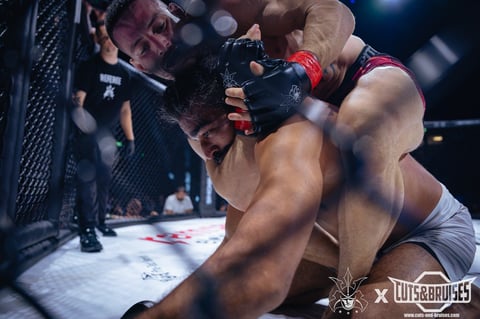 Two MMA fighters grappling inside an octagon cage during a professional mixed martial arts match