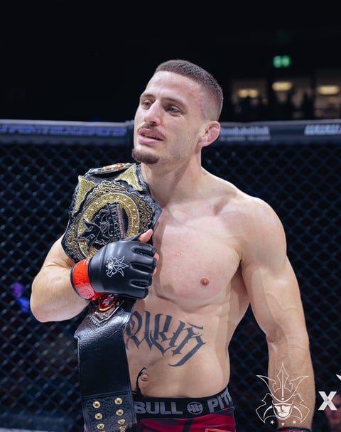 MMA fighter holds championship belt in octagon wearing black gloves and red waistband