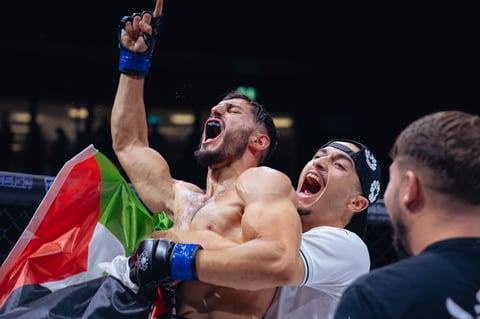MMA fighter celebrates victory with raised fist wearing Italian flag, blue boxing gloves, in competition ring