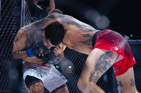 Two MMA fighters grappling against a cage during a mixed martial arts match